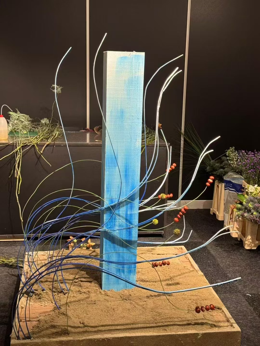 一件蓝色为主的赛事花艺作品，弧形结构、竖向构件与浅色材料共同形成富有方向感的空间关系